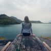 A woman sitting on wooden planks, enjoying a serene mountain lake view.