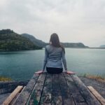 A woman sitting on wooden planks, enjoying a serene mountain lake view.