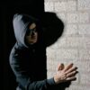 A man in a hoodie hides in the shadows against a brick wall, creating a mysterious mood.