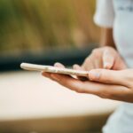 Close-up of a person using a smartphone outdoors, focusing on hands and device.