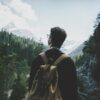 Back view of a man with a backpack hiking through a lush alpine forest in Tirol, Austria.